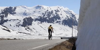 Sykkelturist på fjellvei omgitt av snø, Sunnmøre, en del av trenden Coolcation som forlenger reiselivssesongen på Nordvestlandet.