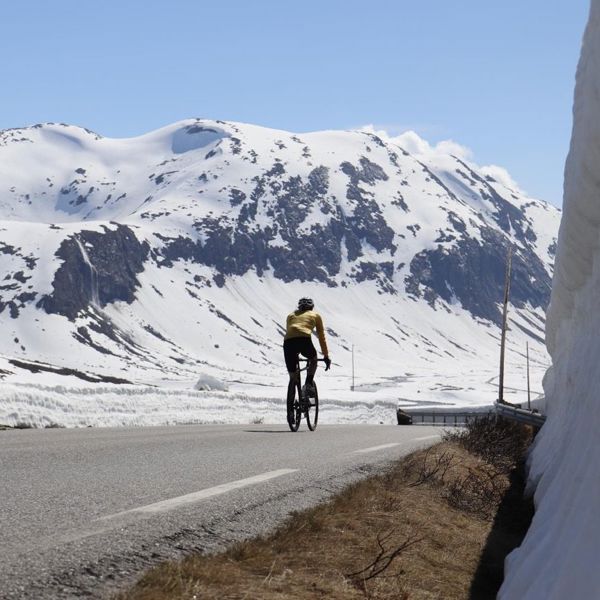 Sykkelturist på fjellvei omgitt av snø, Sunnmøre, en del av trenden Coolcation som forlenger reiselivssesongen på Nordvestlandet.