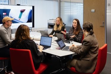 Team i møte om Aidency 113KIT – innovativ medisinsk nødhjelpsløsning. Fem personer diskuterer strategi med bærbare PC-er og en presentasjon på skjerm.