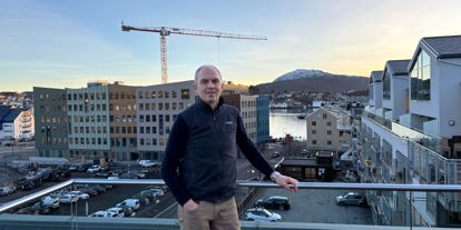 En mann står på en takterrasse med utsikt over et byutviklingsområde med nye bygg, byggekran og nærliggende bebyggelse.