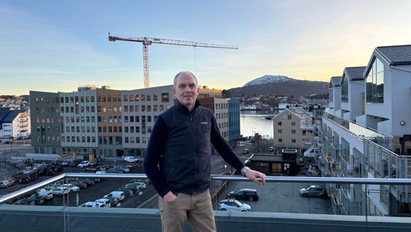 En mann står på en takterrasse med utsikt over et byutviklingsområde med nye bygg, byggekran og nærliggende bebyggelse.