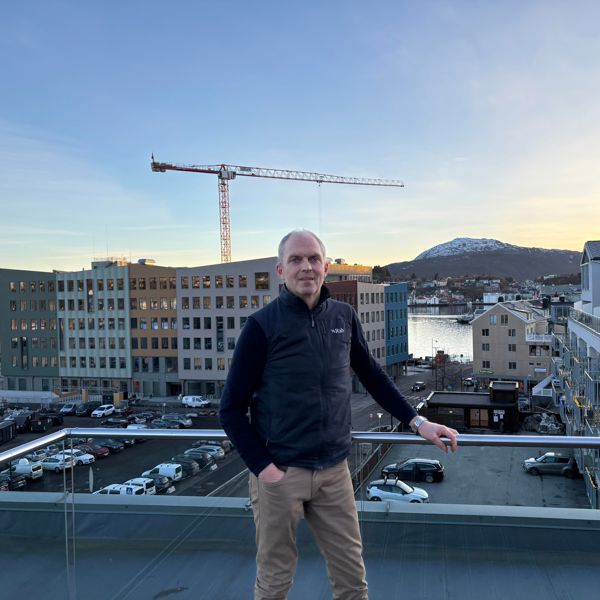 En mann står på en takterrasse med utsikt over et byutviklingsområde med nye bygg, byggekran og nærliggende bebyggelse.