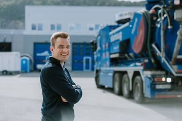 Mann med armene i kryss, stort lagerbygg og renovasjonsbil i bakgrunn