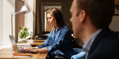 Kvinne sitter ved et skrivebord og skriver på en bærbar PC. 