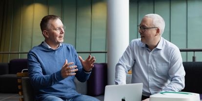 To menn i samtale om Aidency 113KIT – en innovasjon innen akuttmedisinsk støtte. En bærbar medisinsk koffert og en MacBook er på bordet, mens de diskuterer fremtidens akutthjelp.