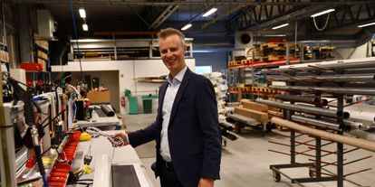 En mann står i produksjonslokalene hos Norsol, ved et arbeidsbord med solskjermingsprodukter og verktøy rundt seg.