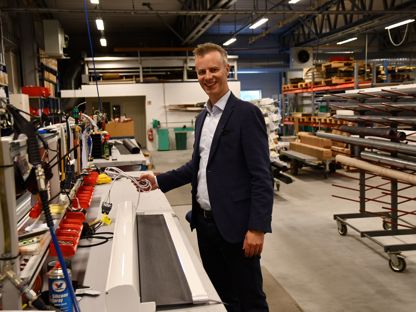 En mann står i produksjonslokalene hos Norsol, ved et arbeidsbord med solskjermingsprodukter og verktøy rundt seg.