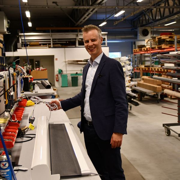 En mann står i produksjonslokalene hos Norsol, ved et arbeidsbord med solskjermingsprodukter og verktøy rundt seg.