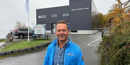 John Henry Holtet, grunnlegger av Storm Elektro smiler i kamera med Storm Elektro bygget i bakgrunnen