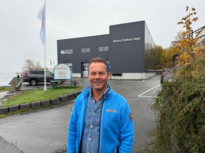 John Henry Holtet, grunnlegger av Storm Elektro smiler i kamera med Storm Elektro bygget i bakgrunnen
