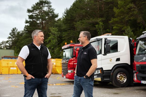 Henrik Wolmer og Odd Arve Hansen i samtale på området til Container Consult, med lastebiler og containere i bakgrunnen.