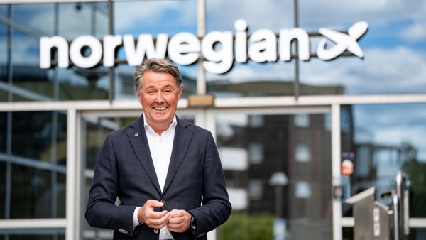 Mann i dress og hvit skjorte står fremfor et forretningsbygg. Norwegian-logo på bygget 