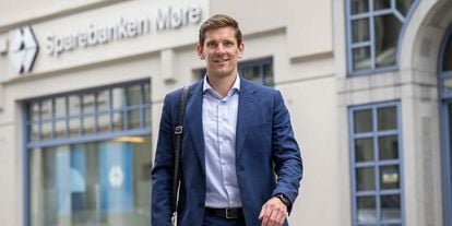 En mann i blå dress smiler til kamera