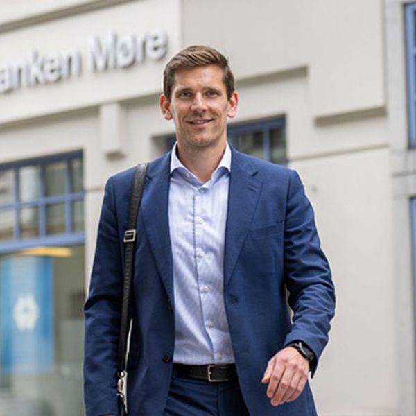 En mann i blå dress smiler til kamera