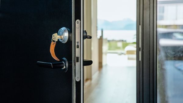 Svart ytterdør som står på gløtt med nøkkelen i. 