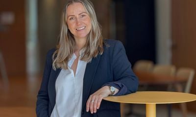 Kvinne sitter på bord, ser inn i kamera med betryggende blikk. Mann står litt bak kvinnen, ser også inn i kamera med betryggende blikk. 