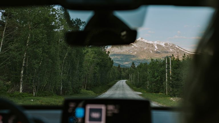 Utsikt til fjell, skog og bilvei fra bil. 