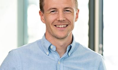 Ung mann kledd i blå skjorte, smiler til kamera