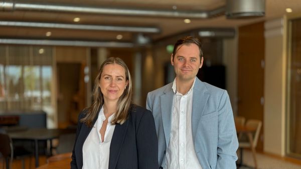 Mann og kvinne i dressjakke og hvit skjorte. Moderne kontorlokaler i bakgrunn 