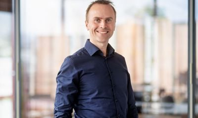 Mann med mørk blå skjorte, smiler og ser i kamera. Blurret bakgrunn. 