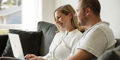 Kvinne og mann som sitter i sofa, med laptop i fanget. 