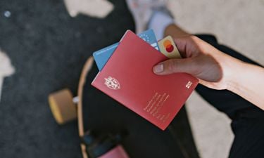 Damehånd som holder pass, kredittkort og europeisk helsetrygdekort i hendene. Vi skimter at hun sitter på et skateboard. 