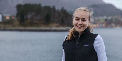 Ung jente som smiler i kamera, ute med hav og natur i bakgrunn