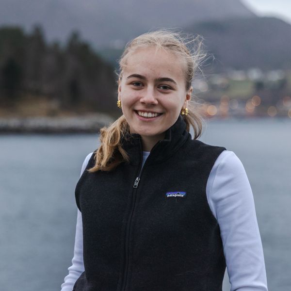 Ung jente som smiler i kamera, ute med hav og natur i bakgrunn