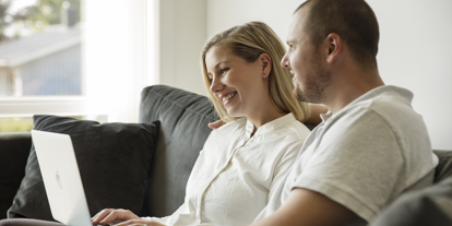 Et par som sitter i sofaen og ser sammen på en laptop. 