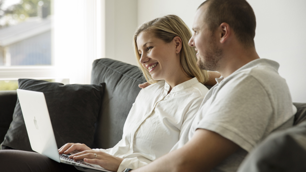 Et par som sitter i sofaen og ser sammen på en laptop. 