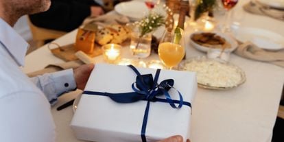 Juledekket bord med en julegave pakket i hvitt papir og blått bånd. 