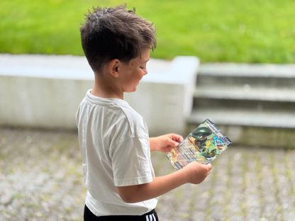 Gutt som står delvis med ryggen til kamera, holder et stor Pokemonkort.  