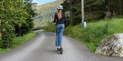 Jente med hjelm på elsparkesykkel på en vei. 