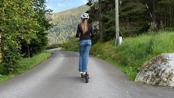 Jente med hjelm på elsparkesykkel på en vei. 