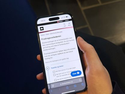 En hånd som holder en mobiltelefon som viser Skatteetaten sine nettsider. 