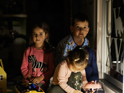 Barn som sitter i mørket med en lampe foran seg. 