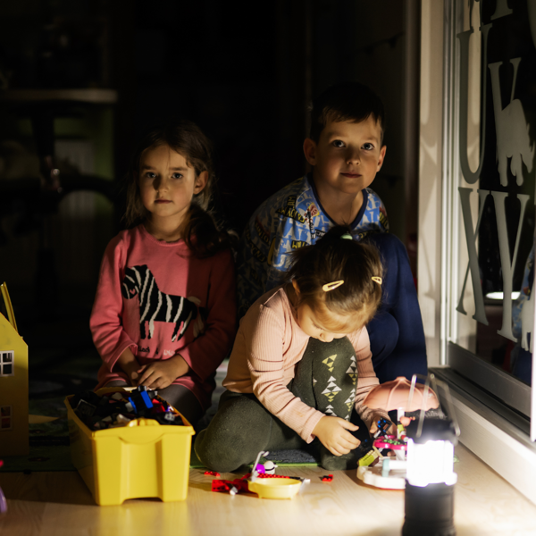 Barn som sitter i mørket med en lampe foran seg. 