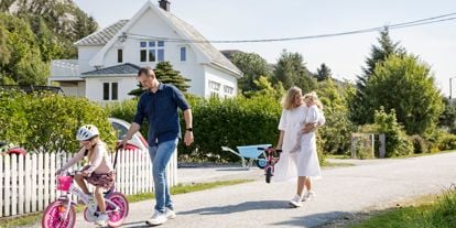 Mann og dame sammen med to små jenter som har med sykkel. Sommerlig antrukket. Hvitt eldre hus i bakgrunn. 