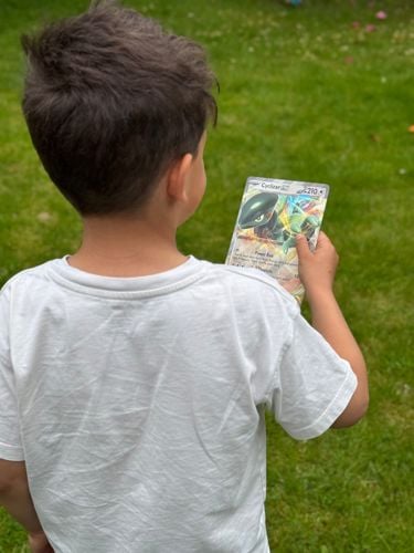 Gutt som står med ryggen til, holder et Pokemonkort i hånden. 