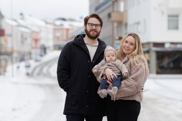 Ungt par i en vinterkledd gate med baby på hånden. 
