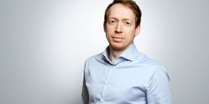 Portrett av Christian Balsnes i lyseblå skjorte mot en lys grå bakgrunn. Han har et rolig uttrykk og ser direkte mot kamera.