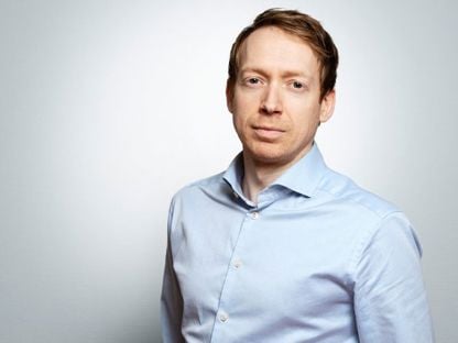 Portrett av Christian Balsnes i lyseblå skjorte mot en lys grå bakgrunn. Han har et rolig uttrykk og ser direkte mot kamera.