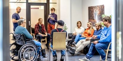 Personer samlet i samtale og veiledning hos Spesialistbedriften. En gruppe mennesker sitter og står i en sirkel i et møterom.