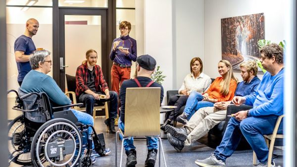 Personer samlet i samtale og veiledning hos Spesialistbedriften. En gruppe mennesker sitter og står i en sirkel i et møterom.