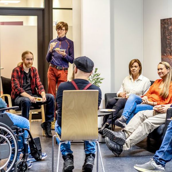Personer samlet i samtale og veiledning hos Spesialistbedriften. En gruppe mennesker sitter og står i en sirkel i et møterom.