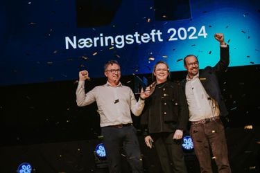 En mann med lys genser, en kvinne med mørkt antrekk og en mann i dressjakke - alle på en scene og jubler over å ha vunnet. Gullkonfetti i luften. 