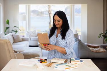 Kvinne sitter ved et bord med fargestifter og tegneutstyr fra Scandinavian Crayon Company. Produktene er utviklet med fokus på kreativ lek og bærekraftige materialer for barn.