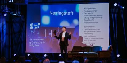 Mann som står på scenen foran et publikum. I bakgrunn vises presentasjon av Næringsteft bak seg. 