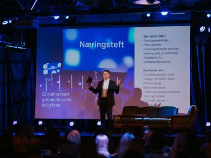Mann som står på scenen foran et publikum. I bakgrunn vises presentasjon av Næringsteft bak seg. 