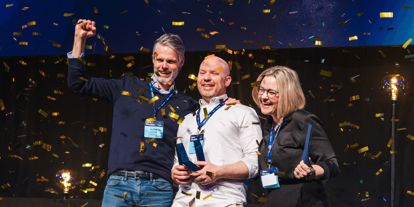 Flere som holder en pokal og jubler, på en scene. Konfetti og god stemning. 